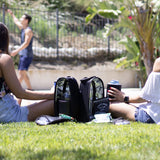 Two sitting on grass watching basketball players with CaddyO Dual Travel Tote